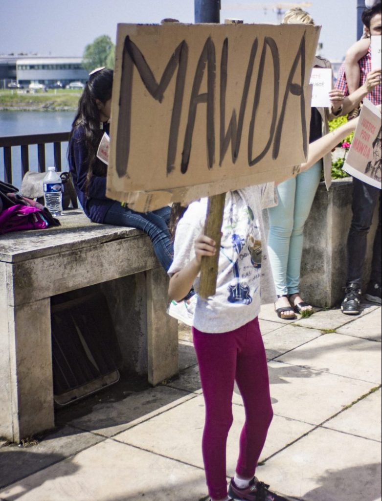 young child holds up a placard with MAWDA written on it