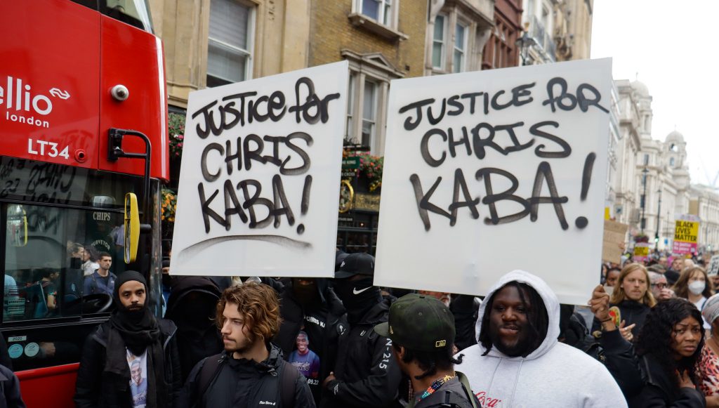 Protesters in central London with banners saying Justice for Chris Kaba. On the left there is a London red bus.