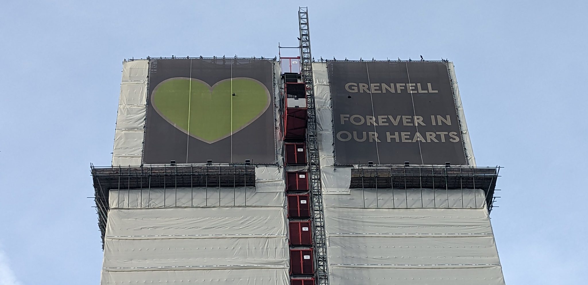 Grenfell Tower draped in memorial green heart and text "Grenfell: forever in our hearts".