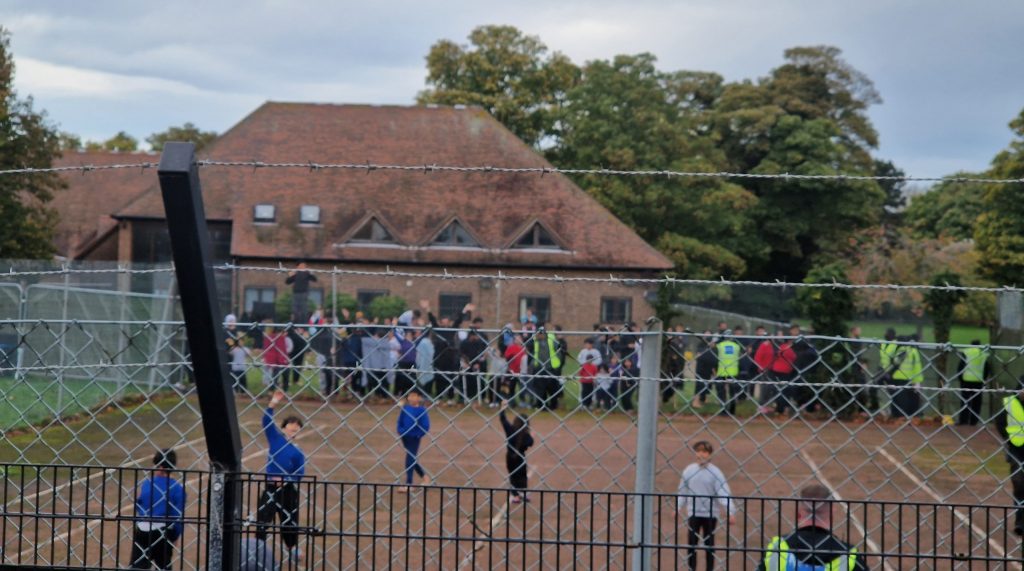 Children behind barbed wire at MAnston camp. More detainees in the background. Some security officers there too.