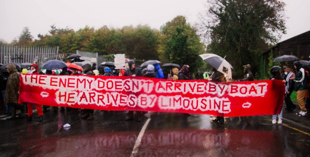 Protesters behind a banner at Manston. Banner reads The enemy doesn't arrive by boat he arrives by limousine
