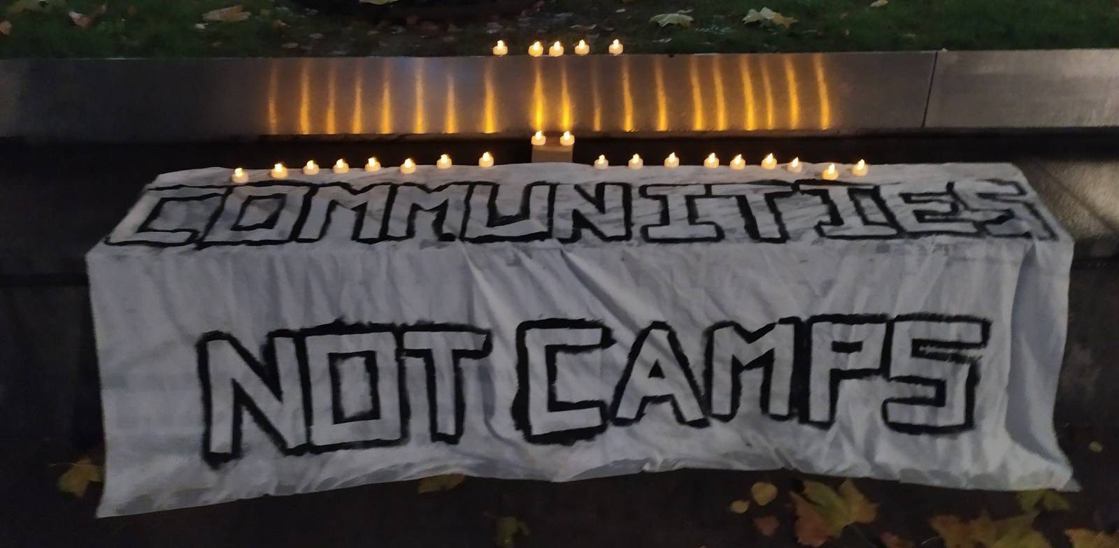 Communities not Camps banner outsider Home Office with candles on top of it
